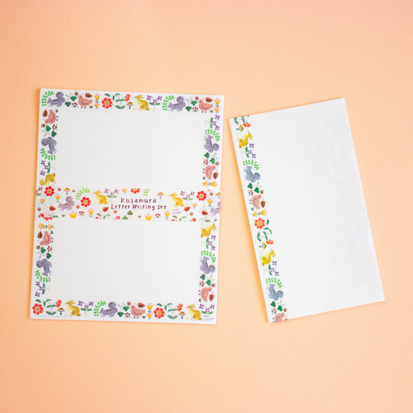 A letterset consisting writing paper sheets and envelopes with colourful illustrated borders featuring birds, flowers, and the text 'kusamura Letter Writing Set' on a peach background.