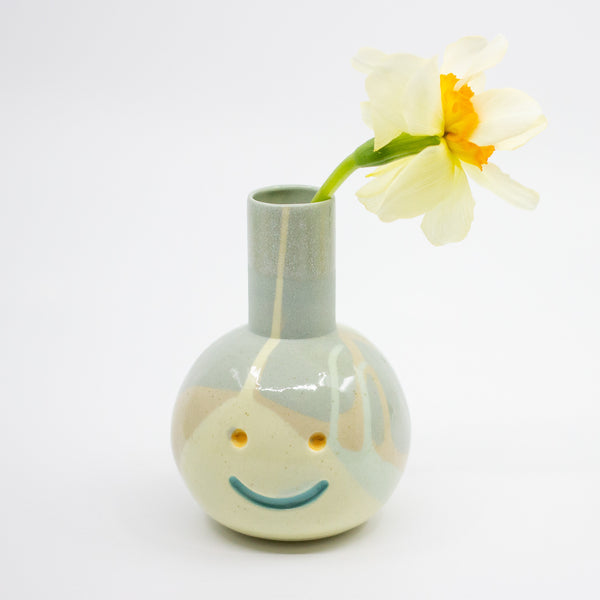 Ceramic vase with a face design holding a flower on a white background