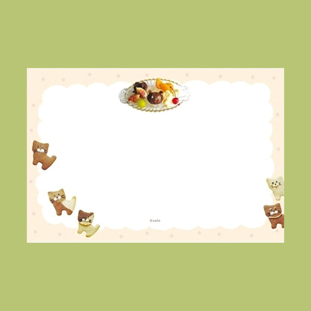 A cute stationery card featuring a scalloped cream border with cat illustrations and a small dessert illustration at the top, set against a light green background.