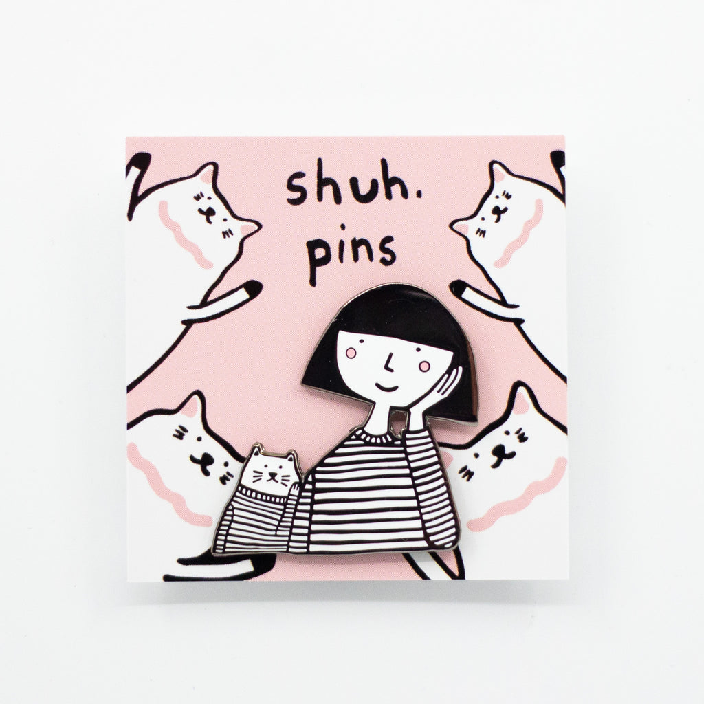 Enamel pin featuring a hand-drawn girl and cat with matching expressions and outfits, displayed on a pink backing card with cat illustrations and “shuh. pins” branding.