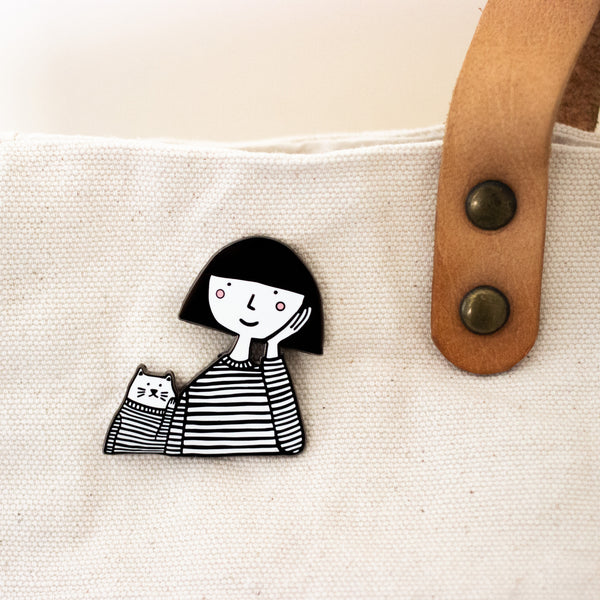 Enamel pin featuring a hand-drawn girl and cat with matching expressions and outfits