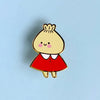 A small enamel pin of a cute cartoon character with a beige head, pink cheeks, a red dress, and a white collar, centered on a light blue background.