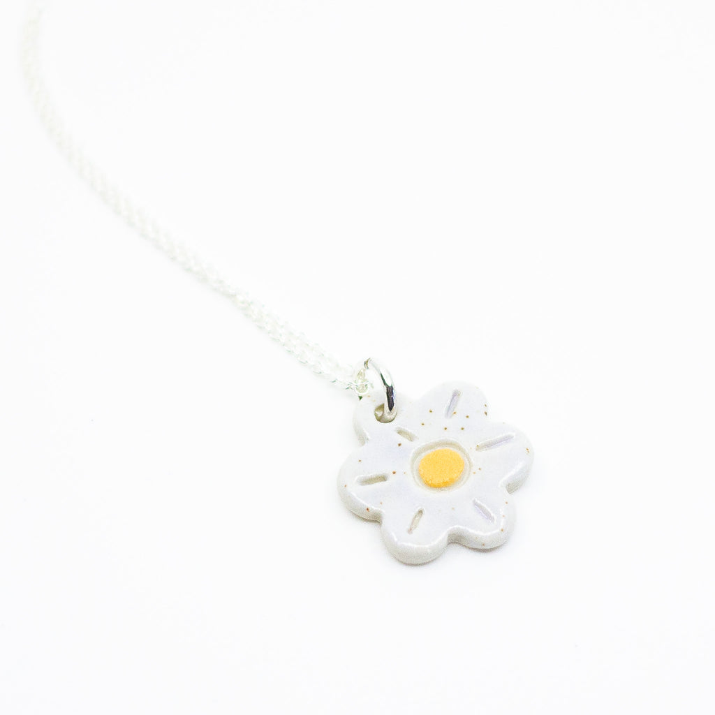 Sterling silver necklace featuring a light white ceramic flower-shaped pendant with a yellow dot in the centre, displayed on a white background.