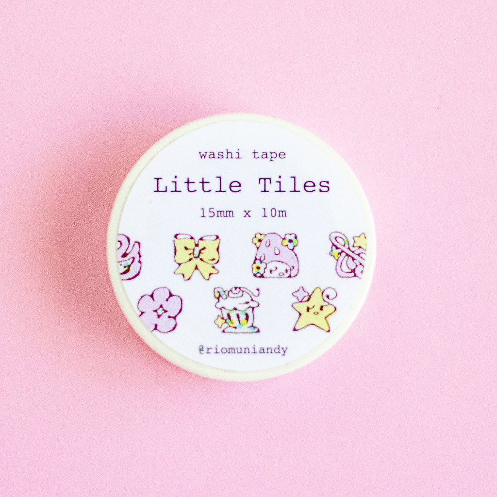 A round container of washi tape labeled 'Little Tiles' by @riomuniandy, featuring cute pastel illustrations of bows, flowers, a cupcake, and stars, set against a solid pink background.
