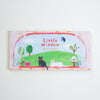 A notepad titled 'Little Window' by Aiko Fukawa, featuring a colourful illustration of a green hill, cats, trees, and a bird under a red dotted border, photographed against a plain white background.