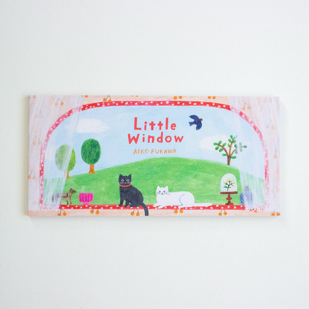 A notepad titled 'Little Window' by Aiko Fukawa, featuring a colourful illustration of a green hill, cats, trees, and a bird under a red dotted border, photographed against a plain white background.