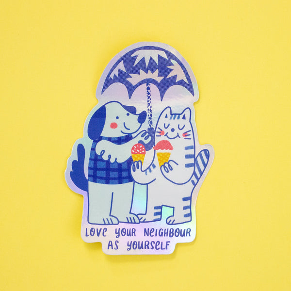A holographic sticker featuring a cat and dog illustration with 'Love Your Neighbour As Yourself' text. 
