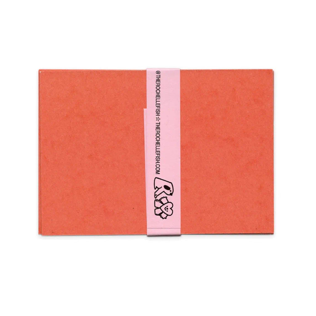 A coral orange backing of the message cards wrapped with a light pink paper band featuring black text and a small cartoon character, shown on a plain white background.