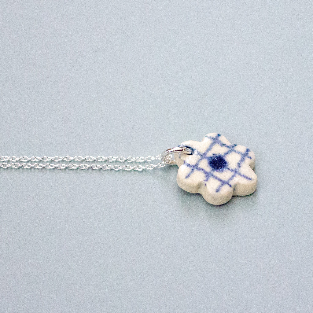 Floral-shaped ceramic pendant on a silver necklace. On a light gray background
