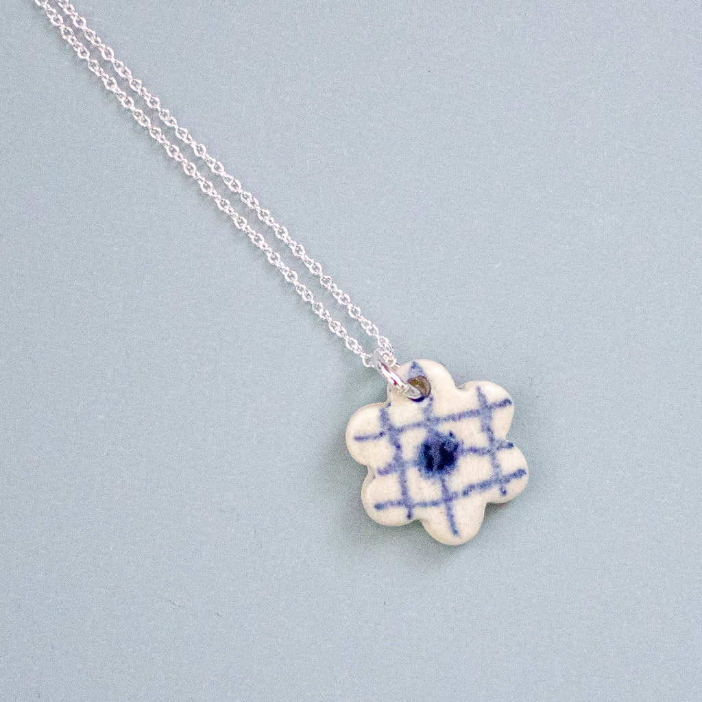 Necklace with a blue and white checkered flower pendant on a light blue background