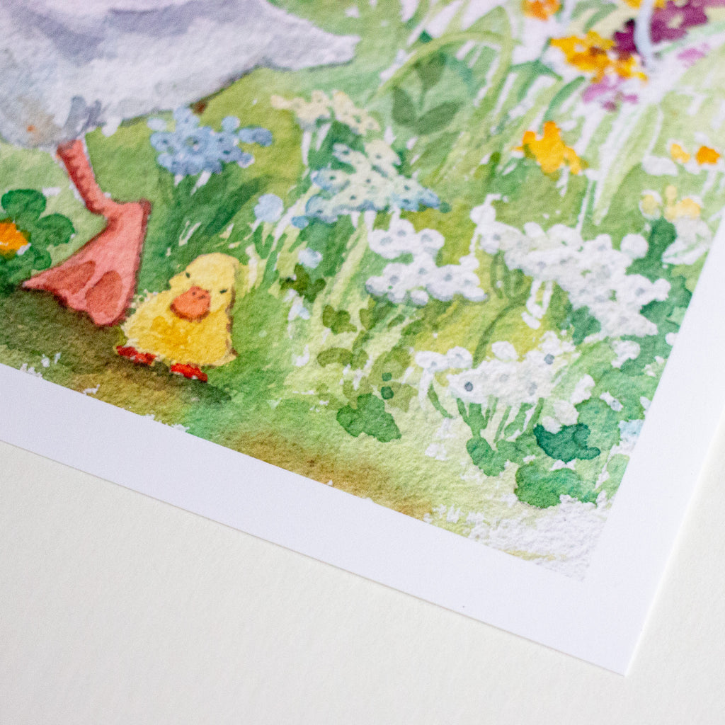 A close-up of a watercolour art print showing a small yellow duckling walking through a green meadow with white and blue flowers.