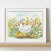 A framed watercolour art print of a mother duck and her ducklings in a flower field, displayed on a light wood shelf against a white wall.