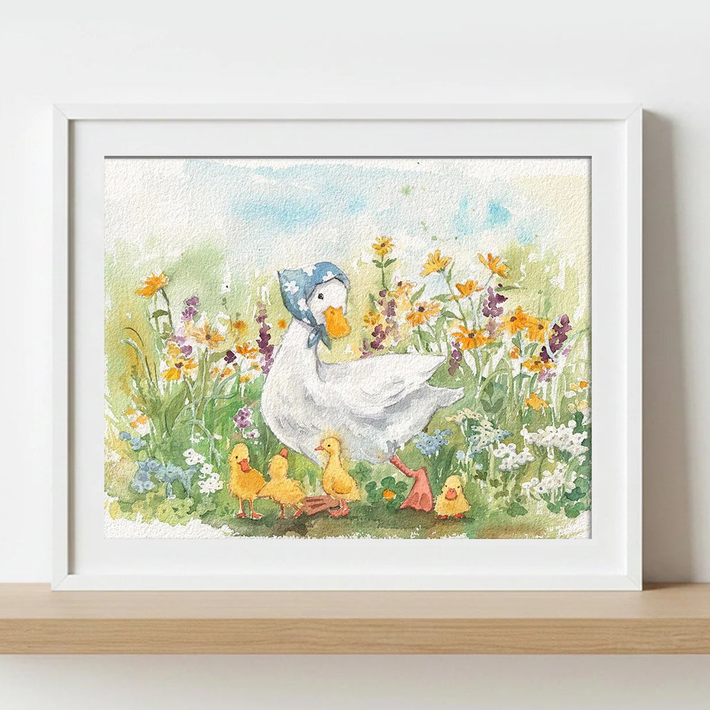 A framed watercolour art print of a mother duck and her ducklings in a flower field, displayed on a light wood shelf against a white wall.