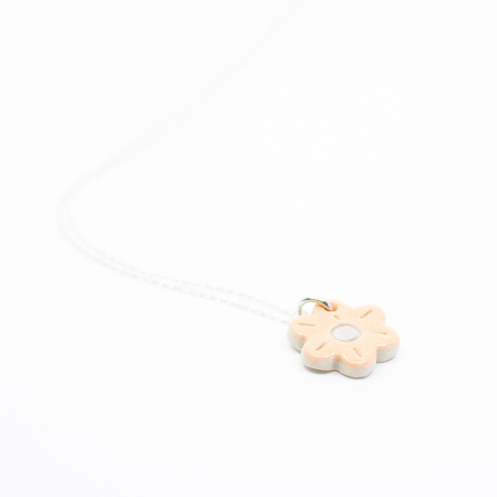 Sterling silver necklace featuring a light peach ceramic flower-shaped pendant with a white dot in the centre, displayed on a white background.