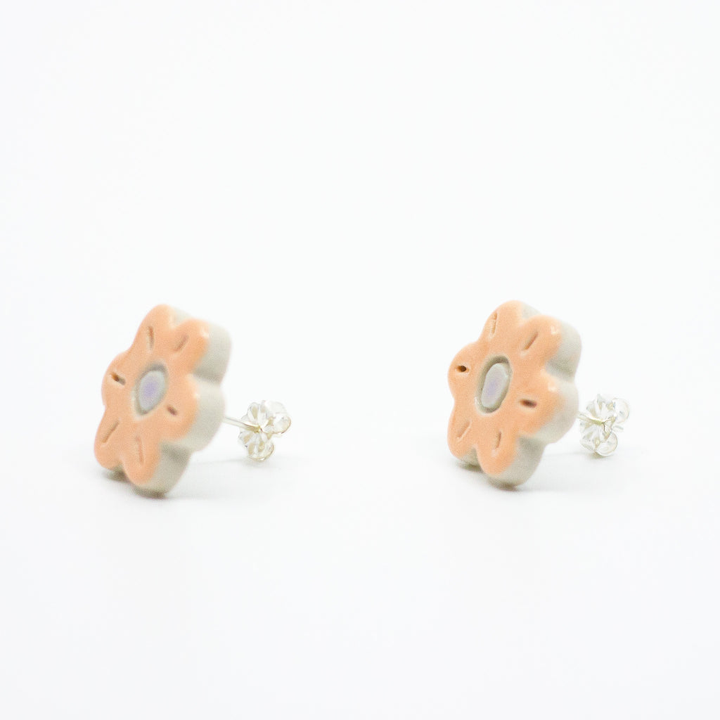 A photo of the marigold stud earrings. Ceramic stud earrings with a flower shape and peach colour leaves with a lilac centre. Side view shows sterling silver stud backing. 