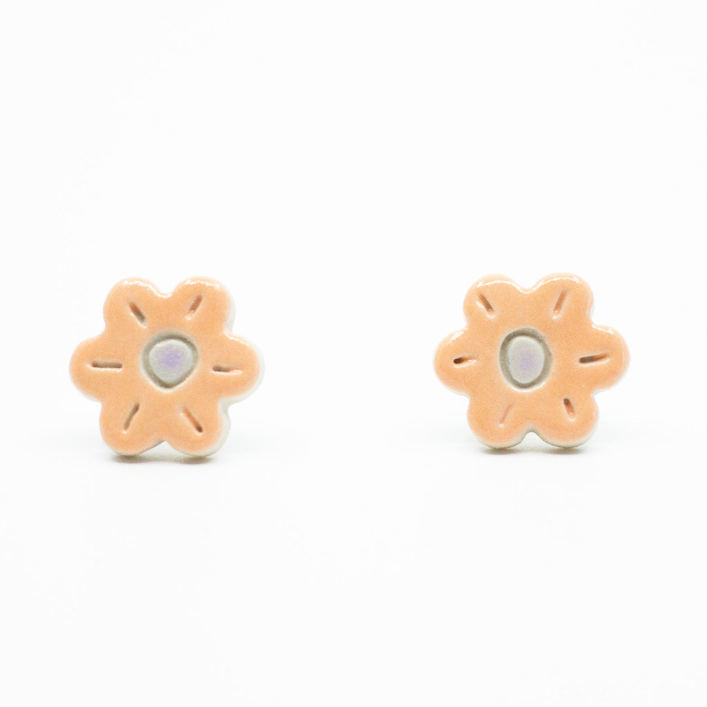 A photo of the marigold stud earrings. Ceramic stud earrings with a flower shape and peach colour leaves with a lilac centre.