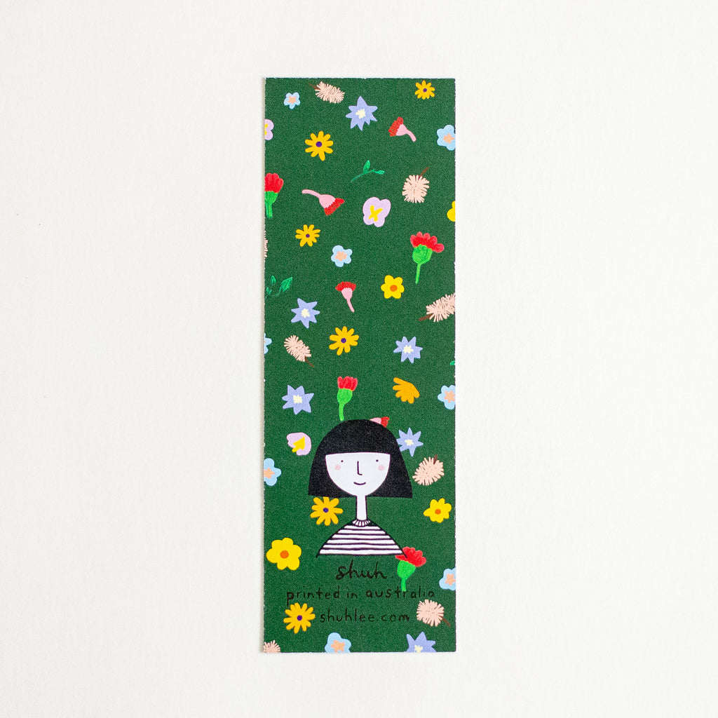 A rectangular green bookmark featuring a colourful floral pattern and a cartoon girl illustration near the bottom, with the text 'shuh. printed in australia' and 'shuhlee.com'.