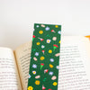 A green book bookmark with a colourful floral pattern, shown spanning open book pages on a white background.