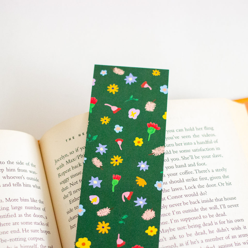 A green book bookmark with a colourful floral pattern, shown spanning open book pages on a white background.