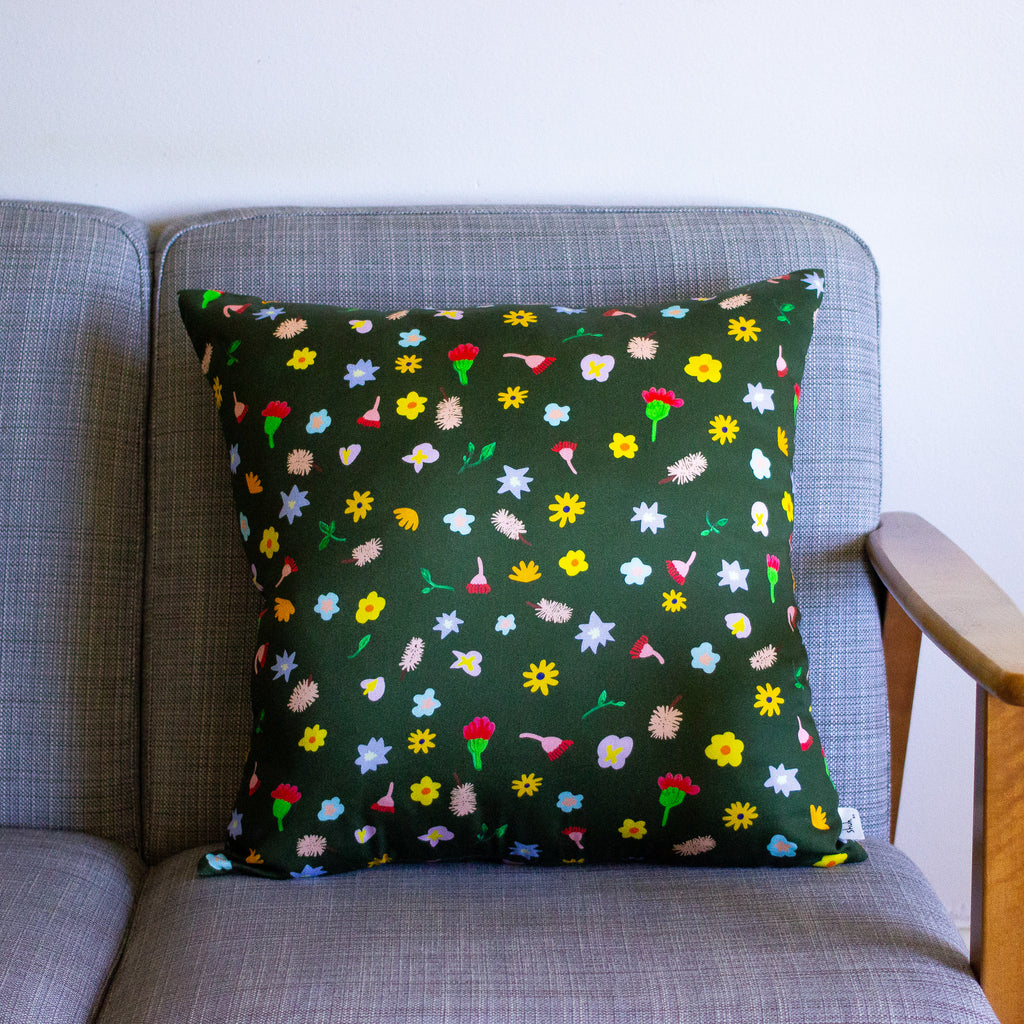 A Front view of the meadow cushion cover on a couch. Multicoloured and varied flowers on a dark green background. 