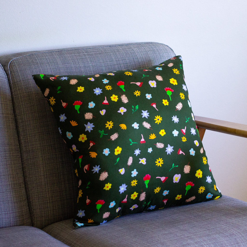 A Front view of the meadow cushion cover on a couch. Multicoloured and varied flowers on a dark green background. 