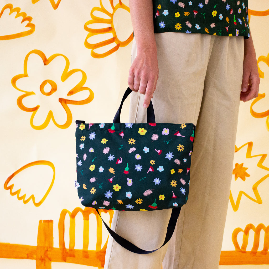 The meadow easy bag being carried as a tote. Multicoloured flowers on a meadow green background.