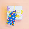 A gift tag with colourful floral and abstract patterns on a blue background attached to a yellow string on a gift box.