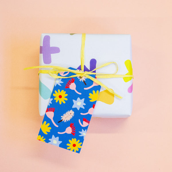 A gift tag with colourful floral and abstract patterns on a blue background attached to a yellow string on a gift box.