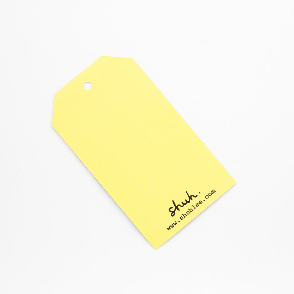 Yellow tag with 'shuh.' branding on a white background