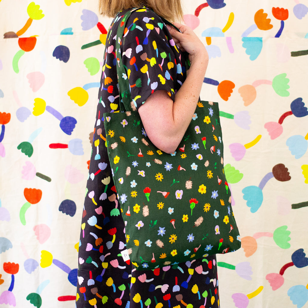 A side view of the meadow linen tote being carried by a model on their shoulder. Illustrated flowers on a meadow green 