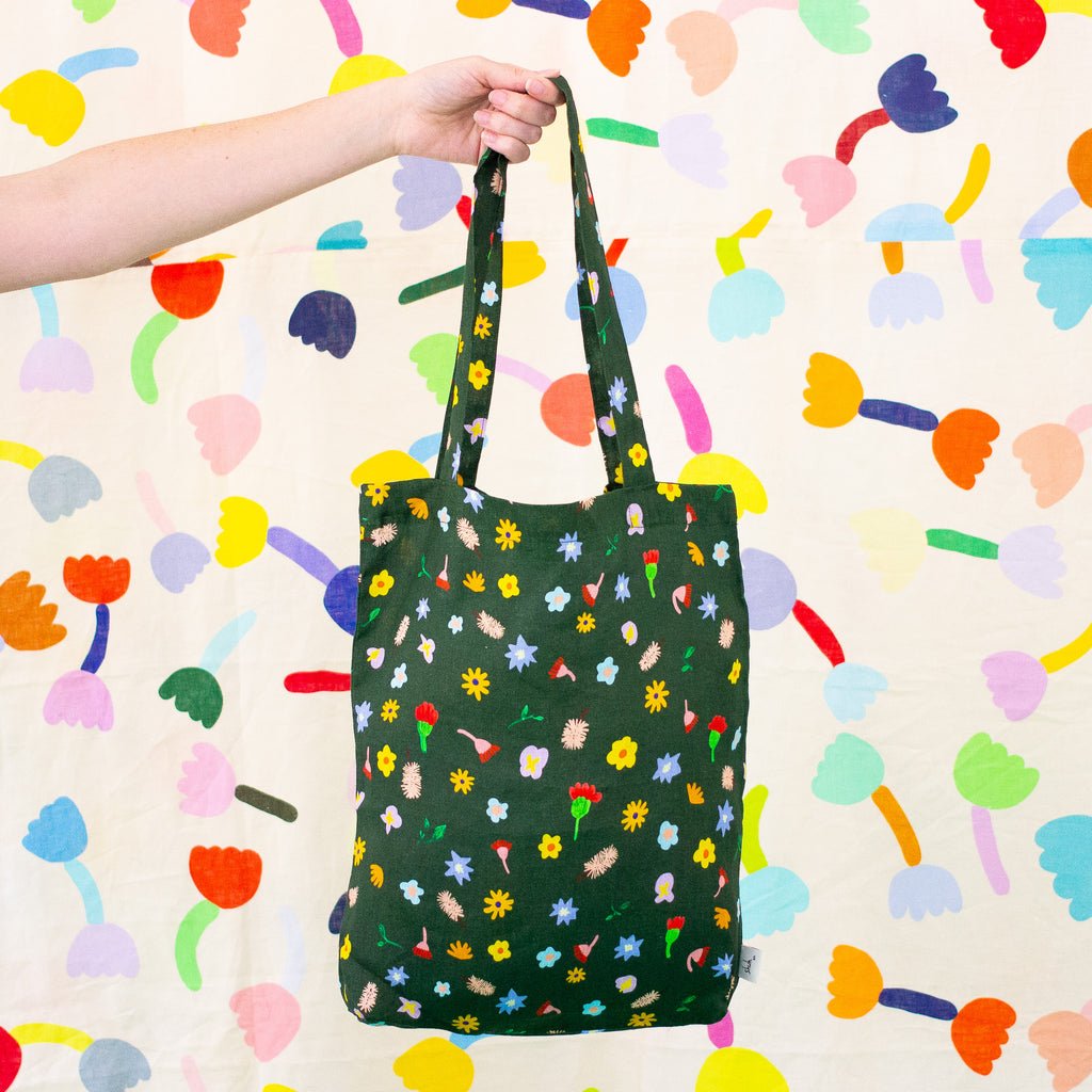 A picture of the meadow linen tote being held up by a hand. Illustrated flowers on a meadow green background. 