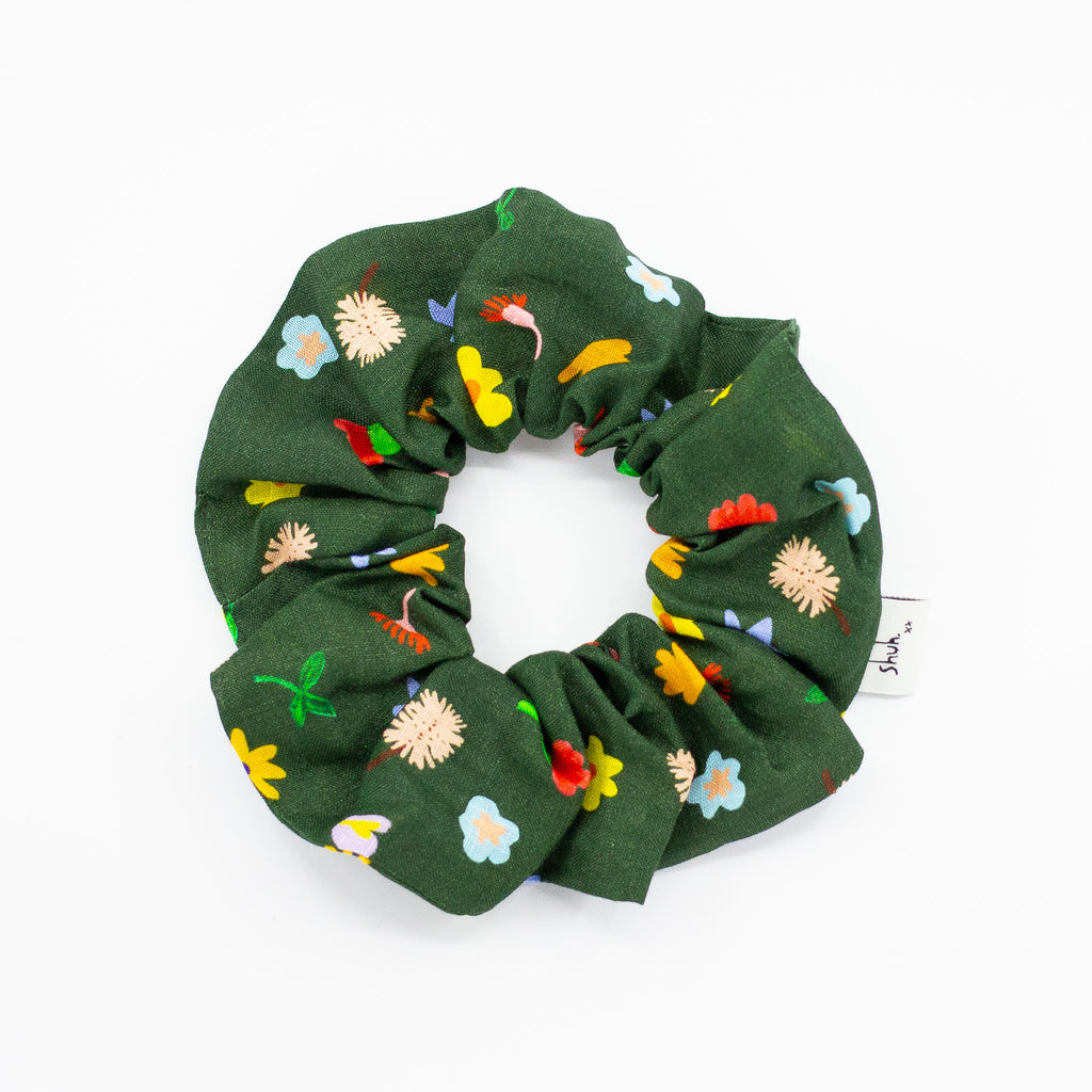 Dark green fabric scrunchie featuring a colourful floral print with red, yellow, blue, and cream flowers, arranged in a circular shape on a white background.