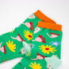 A Closeup view of the Meadow socks collar. Green background, multicoloured wildflowers, and orange toe with mint heel. 