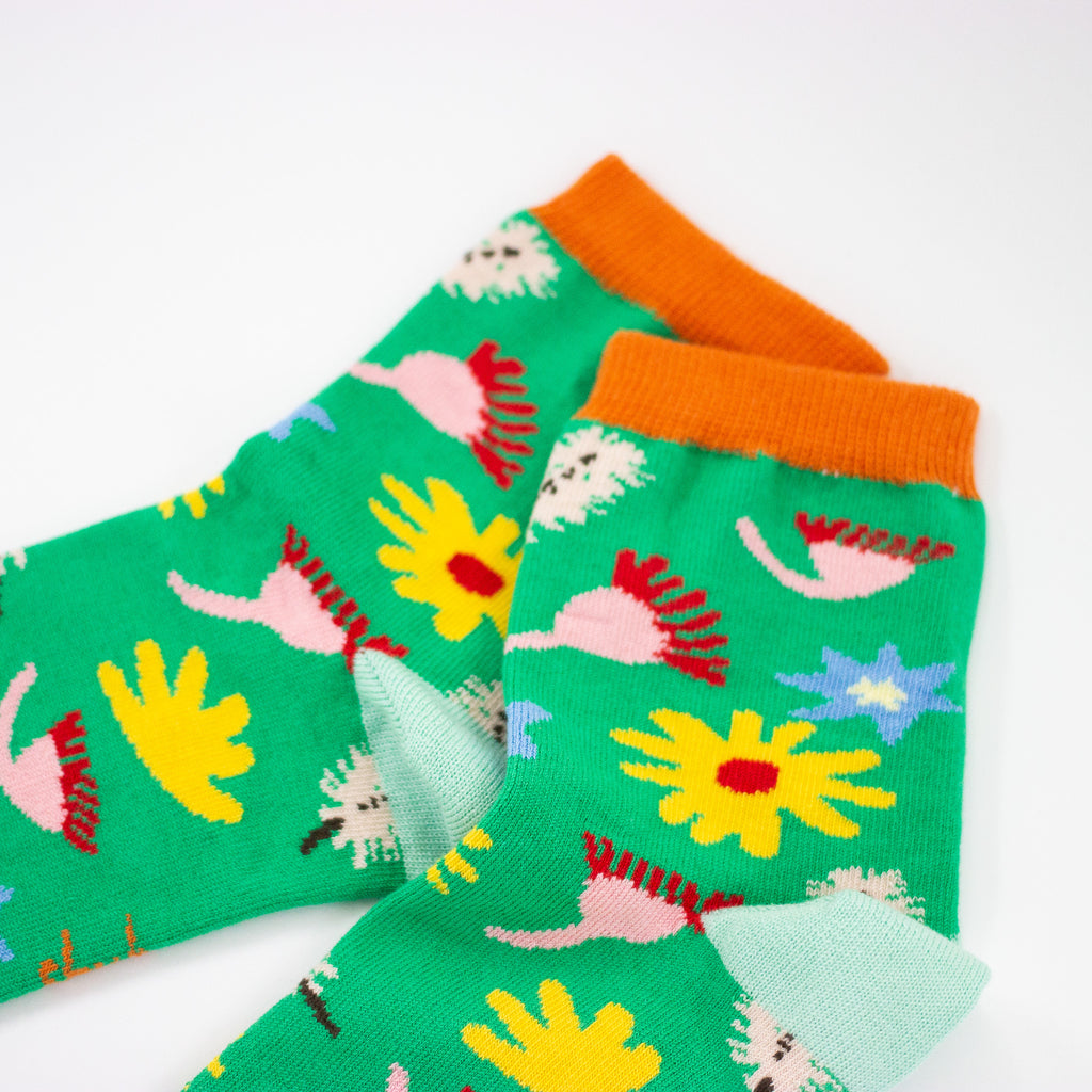 A Closeup view of the Meadow socks collar. Green background, multicoloured wildflowers, and orange toe with mint heel. 