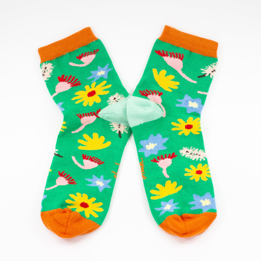 Front view of the Meadown socks. Green background, multicoloured wildflowers, and orange toe with mint heel. 