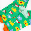 A Closeup view of the Meadown socks heel. Green background, multicoloured wildflowers, and orange toe with mint heel. 
