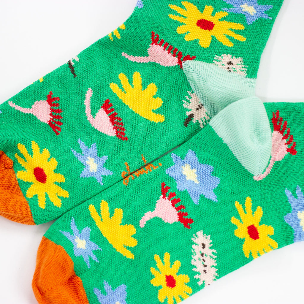 A Closeup view of the Meadown socks heel. Green background, multicoloured wildflowers, and orange toe with mint heel. 