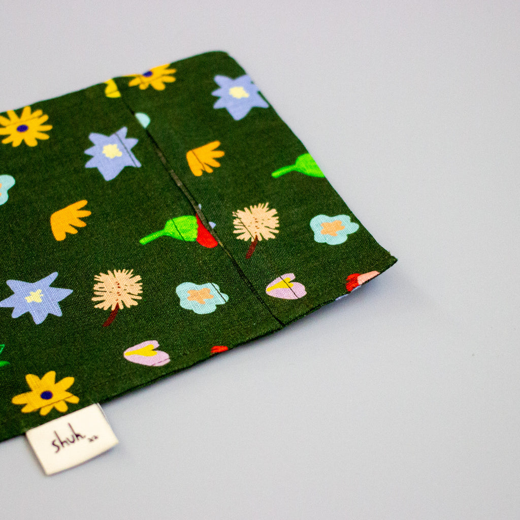 Fabric with colourful floral pattern on a green background, featuring a 'shuh' label.