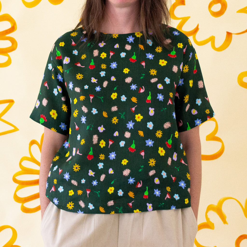 A Front view of a model wearing the Meadow linen top. Various flower designs over a meadow green background. 
