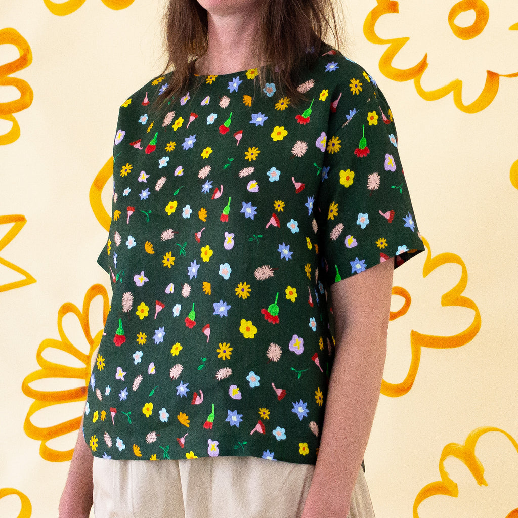 A side view of a model wearing the Meadow linen top. Various flower designs over a meadow green background. 