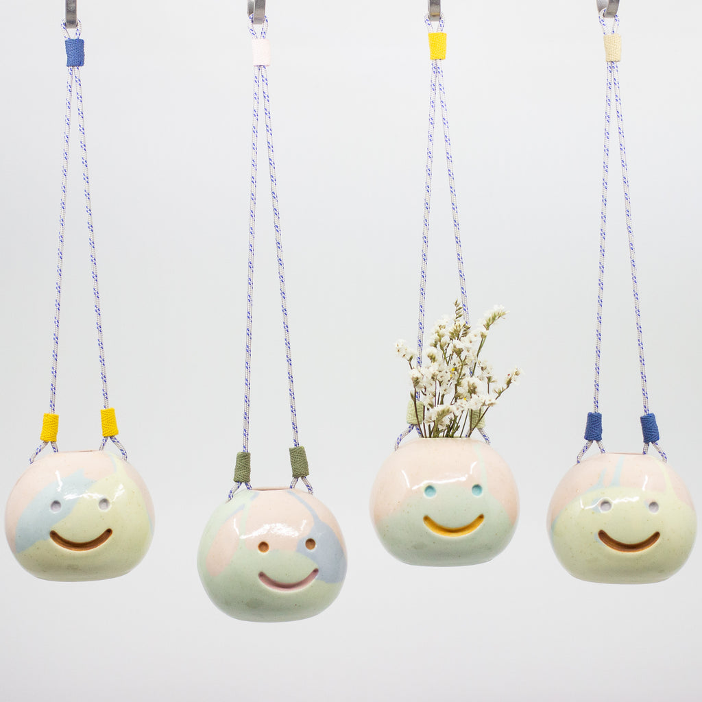 Four ceramic hanging planters with smiling faces on a white background