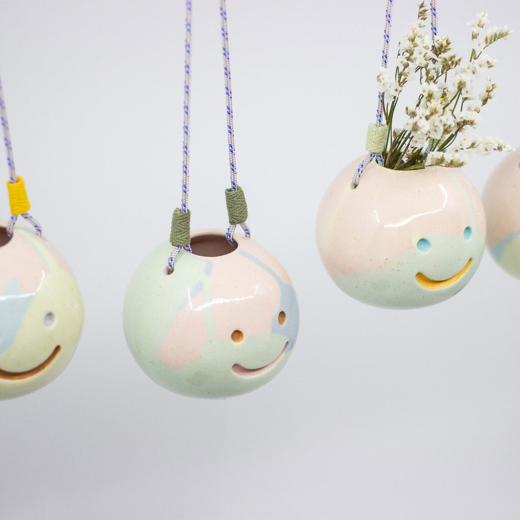 Set of hanging ceramic planters with smiley face designs on a light gray background