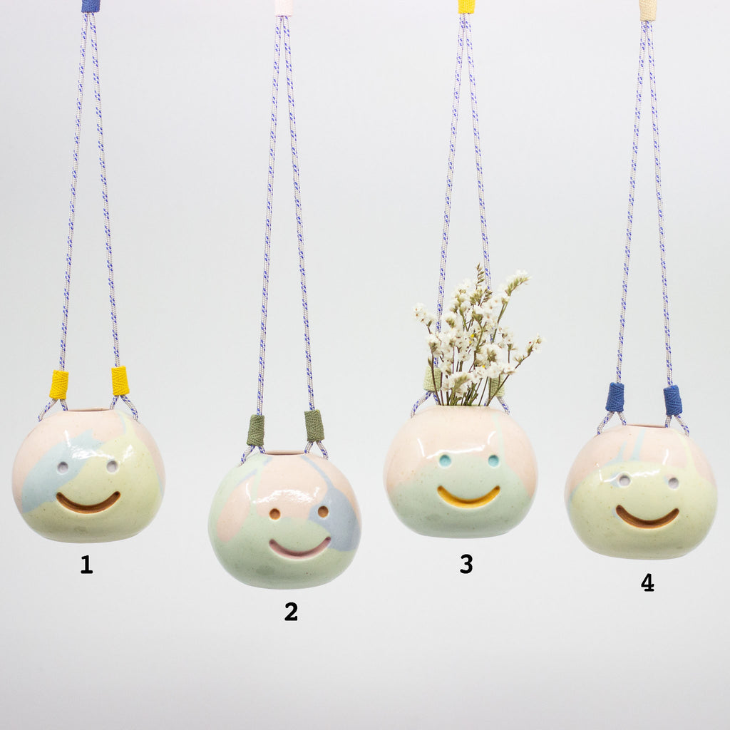 Four ceramic hanging planters with smiley face designs on a white background