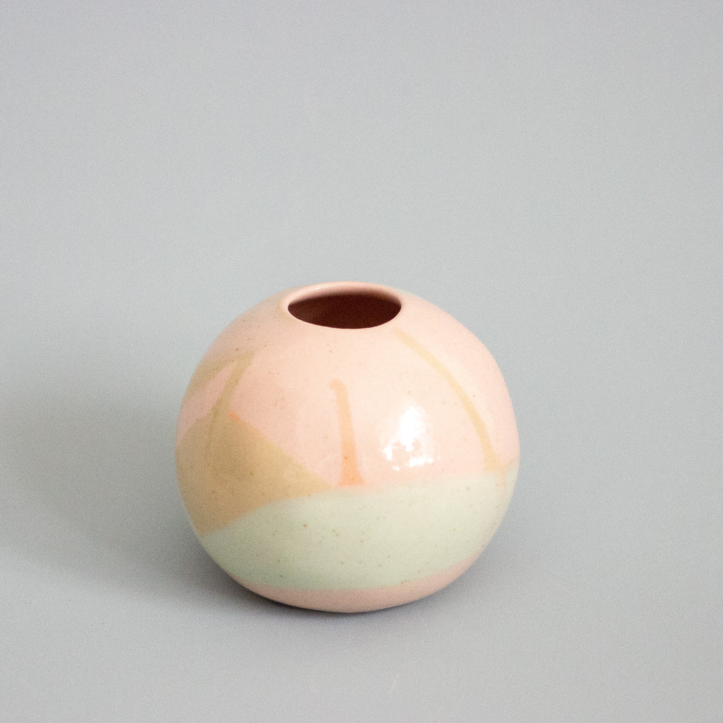 Round ceramic vase with two-tone peach and mint design on a gray background