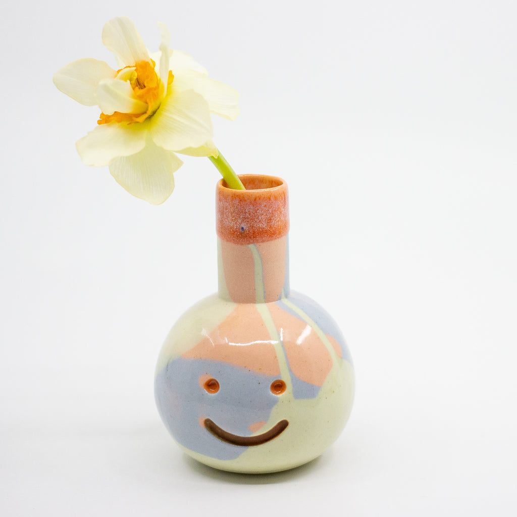 Ceramic vase with a face design holding a flower on a white background