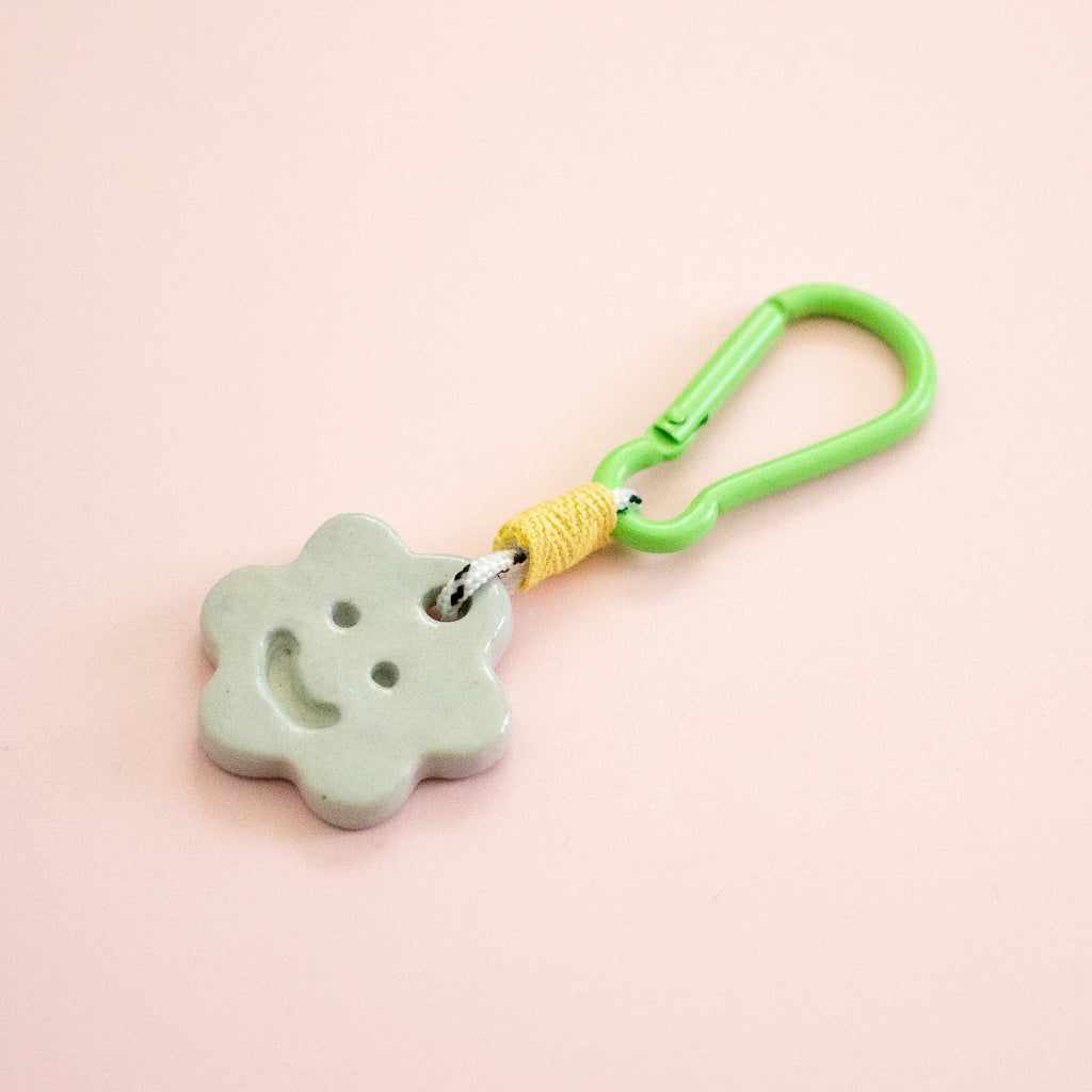 Green keychain with a smiley face charm on a pink background