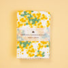 A folded white handkerchief with a yellow and green floral pattern, wrapped in a paper band that reads 'HAIKARA HANDKERCHIEF made in JAPAN', set against a solid pale yellow background.