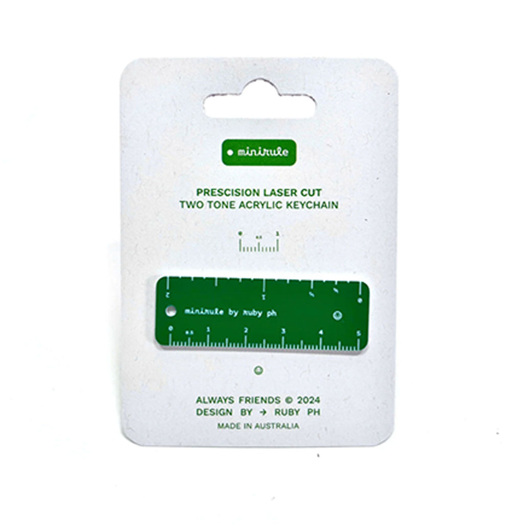 A green acrylic keychain ruler with white markings, mounted on a white retail card with the brand name 'minirule' and product text.