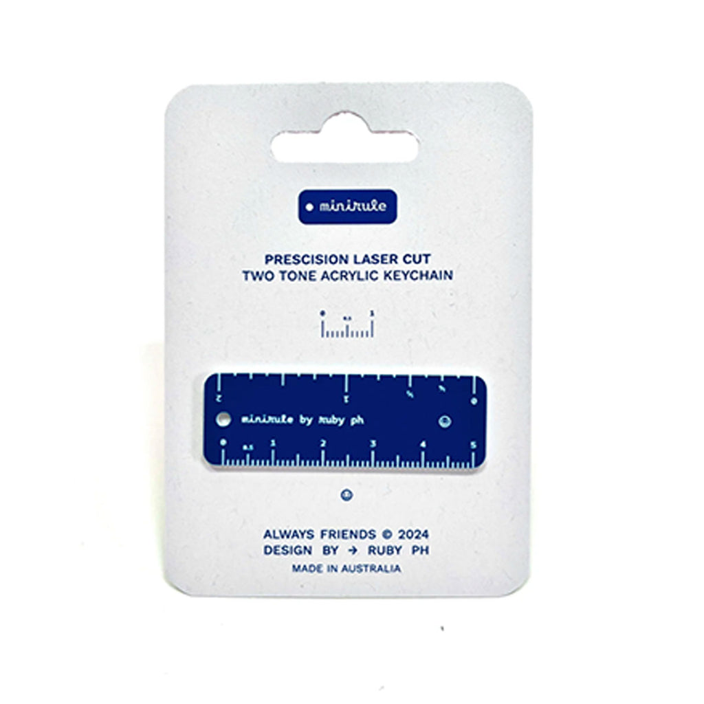 A precision laser-cut two-tone acrylic keychain ruler, shown in its original white cardboard packaging with blue text and branding.