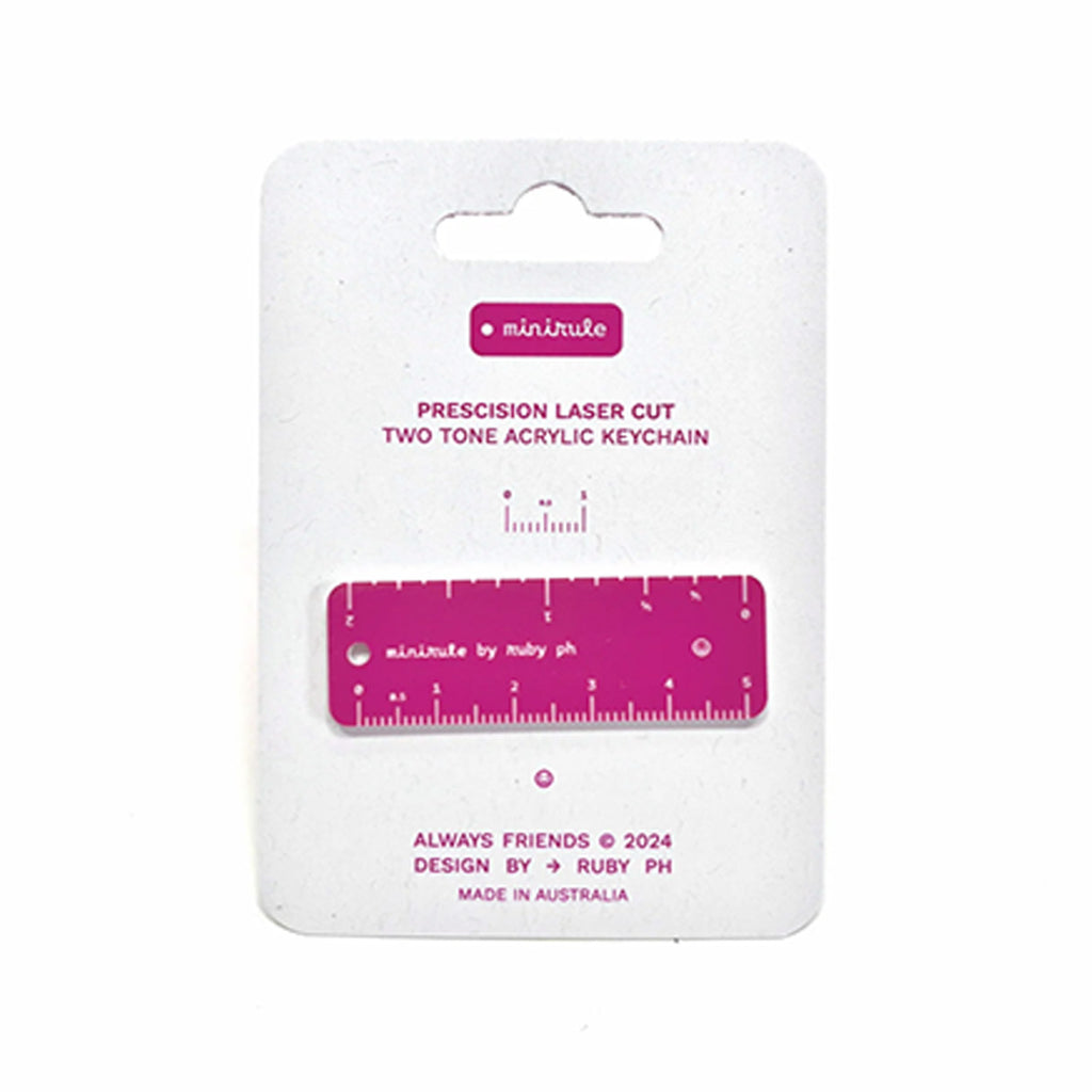 A two-tone acrylic keychain ruler in magenta and white, mounted on a white cardboard hanger card with printed product details.
